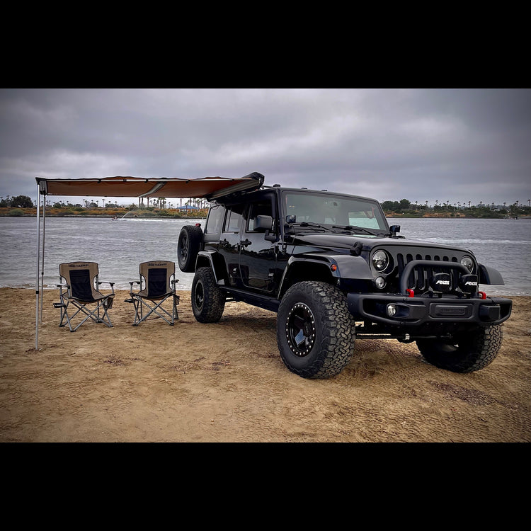 Black Jeep Wrangler overland camping on beach with ARB awning and chairs in tan